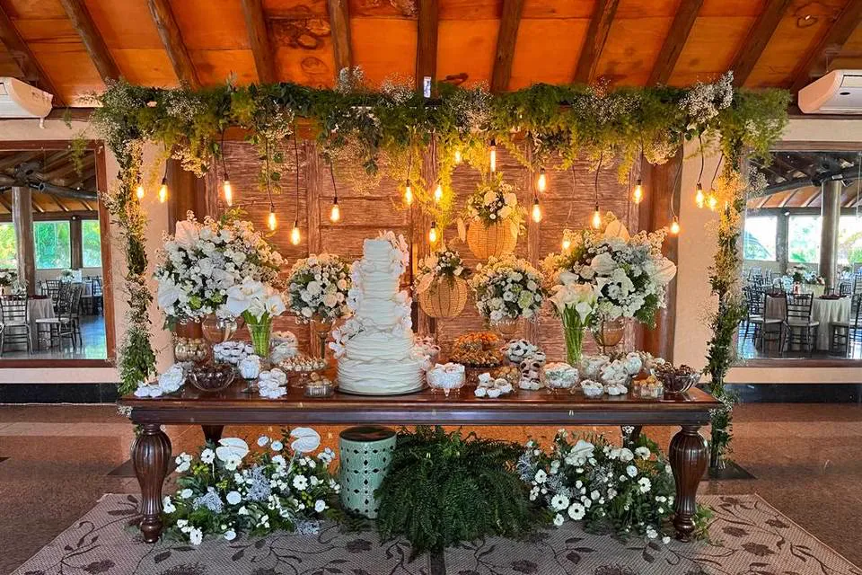Mesa de bolo sob pergolado com arranjos florais